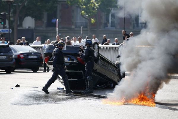 Policiais franceses so vistos perto de carro capotado em greve de taxistas em Paris nesta quinta-feira (25)