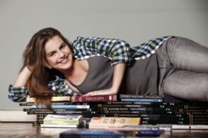 Bianca Salgueiro posa em cima de pilha de livros em sua casa
